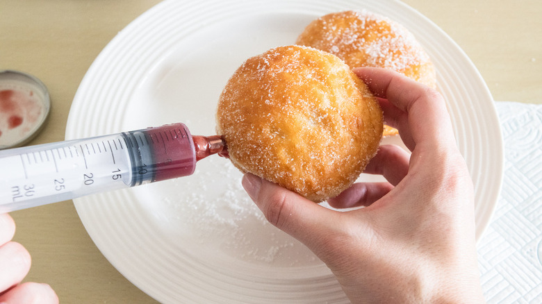 sugary donuts being filled with seedless raspberry jam in a syringe