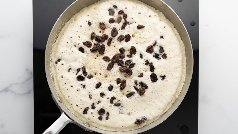 Pancake batter and raisins in pan