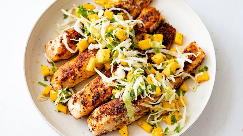 Four salmon filets on a white plate with slaw on top