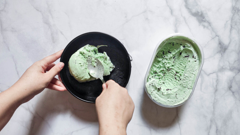 hands scooping mint ice cream from container into bowl