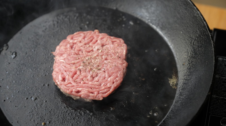 Beef patty cooking in cast-iron pan