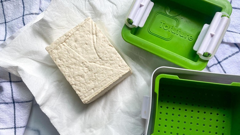 Tofu press and block of tofu on paper towels