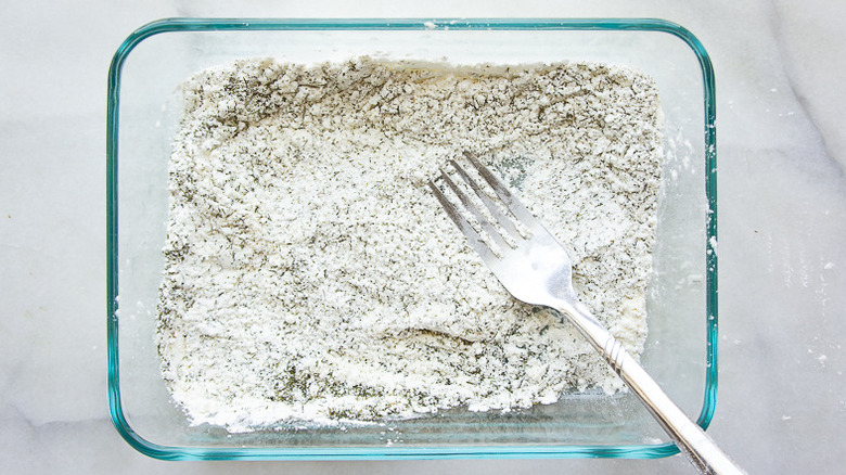 a bowl of flour and cornstarch with dried dill mixed together