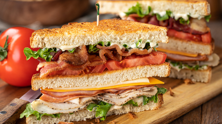 closeup of club sandwich cut in half with tomato in background