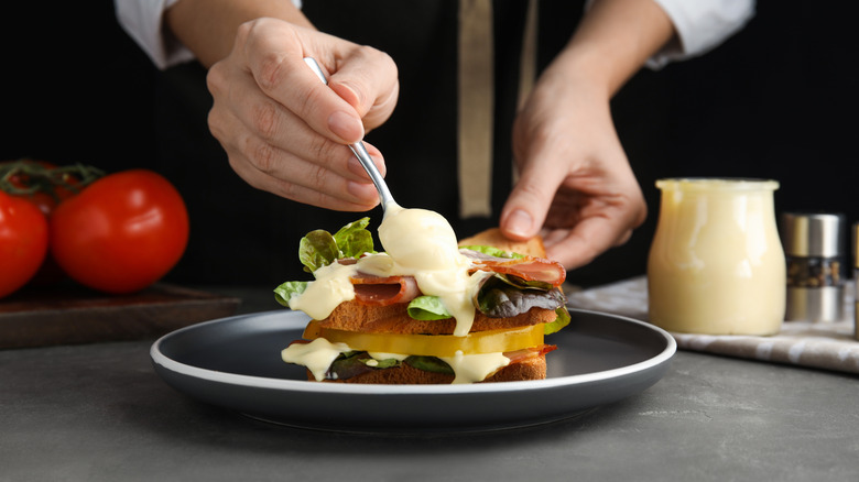 a person adding mayonnaise to a club sandwich in an artsy setting