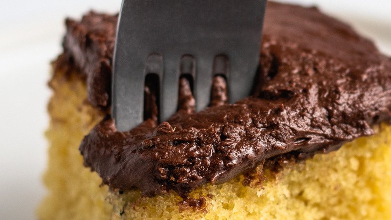 Fork in square of yellow cake with thick chocolate frosting