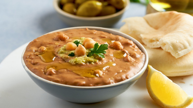 Bowl of ful medames with bread and lemon wedge