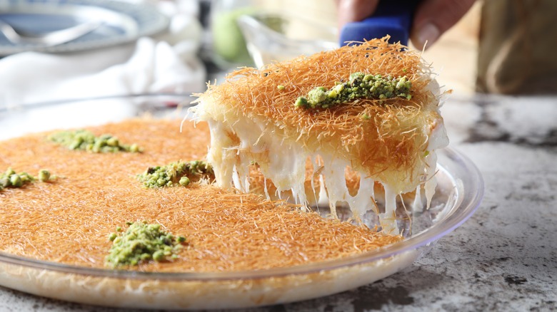 A slice of knafeh being lifted from a platter