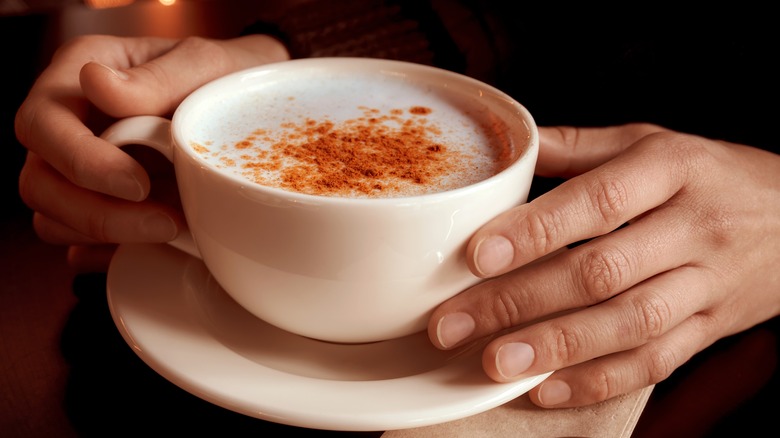 Hands holding cup of sahlab dusted with cinnamon