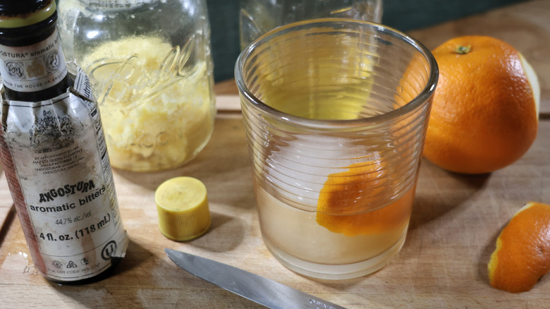 butter-washed Old Fashioned with orange peel on cutting board with bitters, orange, and jars