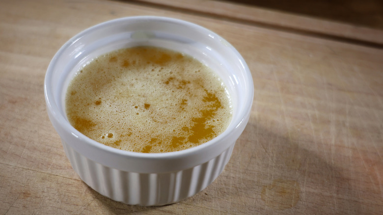 a ramekin full of melted butter sitting on a cutting board