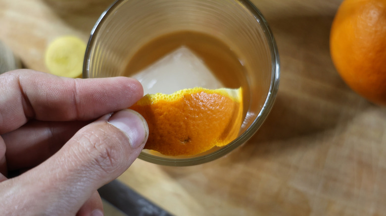 fingers placing a slide of orange peel into a rocks glass full of cocktail and ice