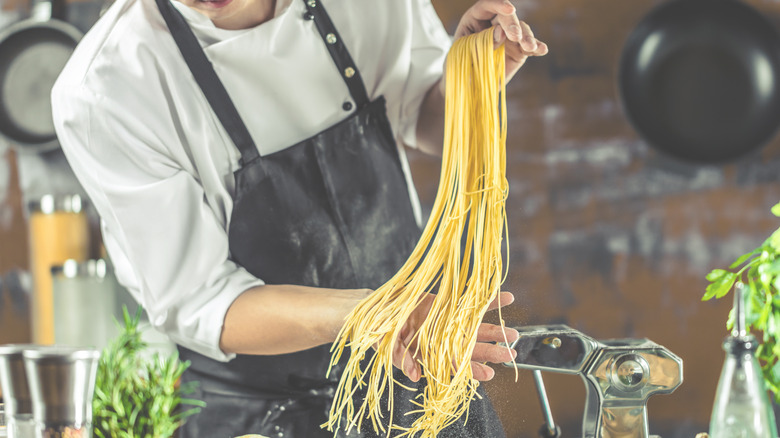 A chef holding long spaghetti noodles