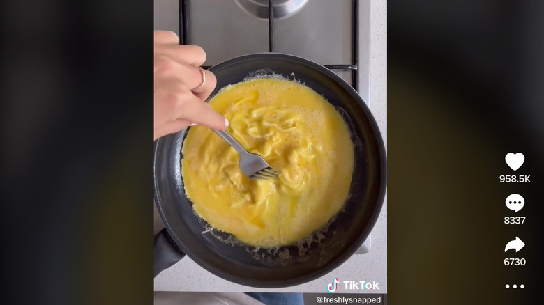 A TikToker folding eggs with a metal fork 