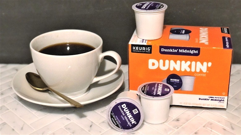 a cup of coffee sitting nex tto the Dunkin' donuts dunkin' midnight box of k-cups coffee