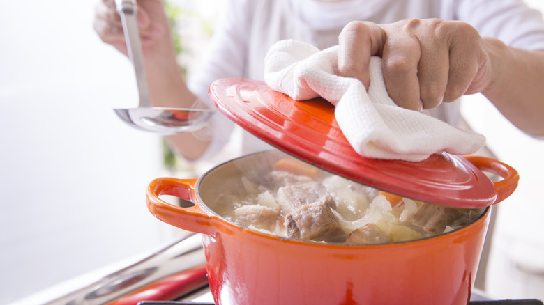 Woman lifting top of Dutch oven pot on stove with ladle