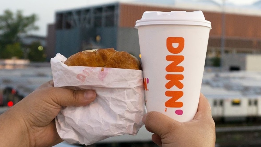 Hands holding Dunkin' breakfast sandwich and coffee