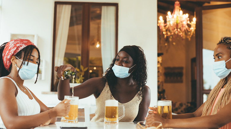 Three women in masks drinking beer