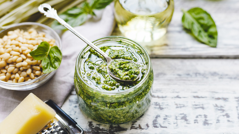 Pine nuts in bowl next to jar of pesto with spoon