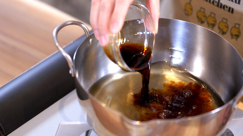 Hand pouring soy sauce into a stainless steel pot