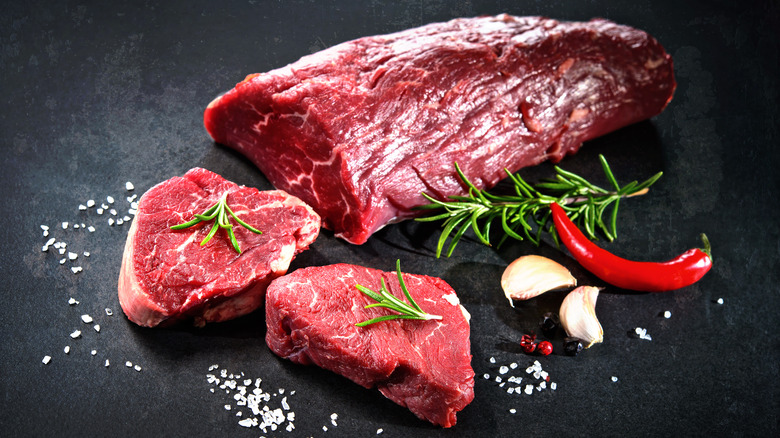 Tenderloin on black surface with pepper, salt, and garlic