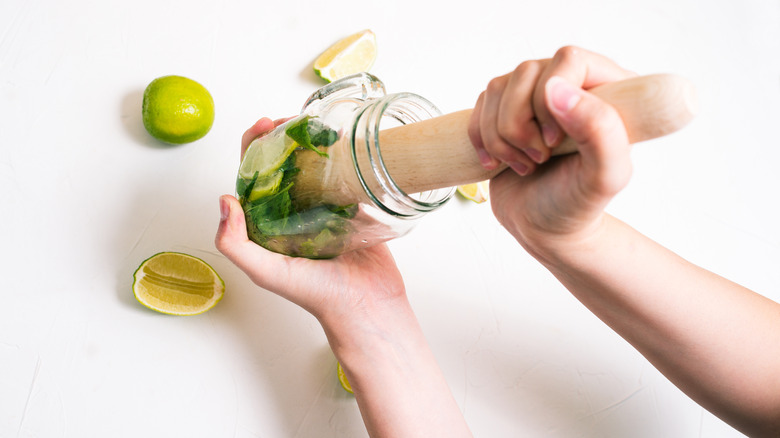 Person muddling lime in glass