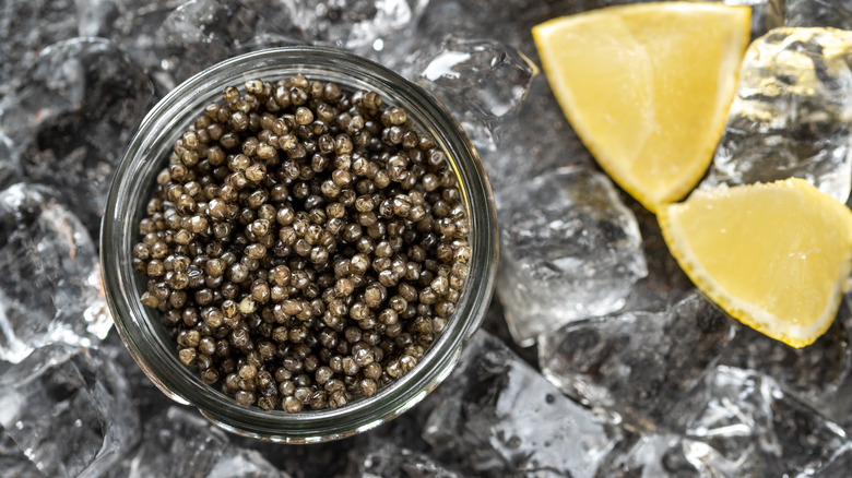 A bowl of caviar on ice with lemon wedges