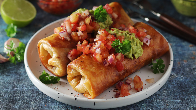 Two chimichangas with salsa and guacamole on plate