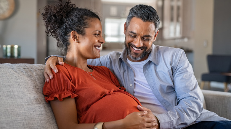 A pregnant woman and her partner smiling and holding her bump