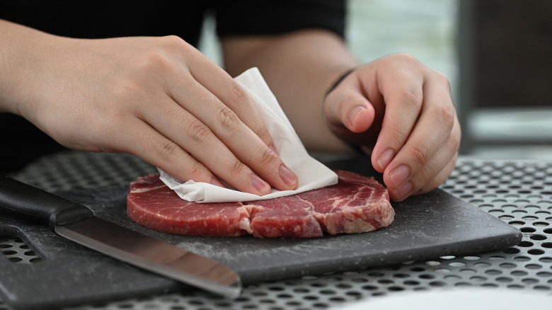 Hands patting a raw steak with a paper towel