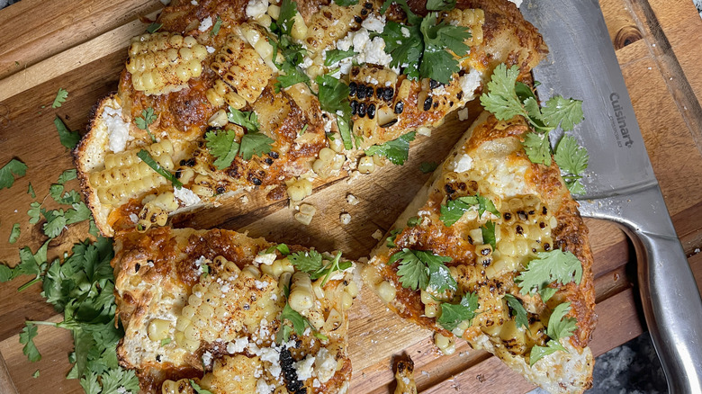 sliced cheesy elotes street corn pizza on cutting board