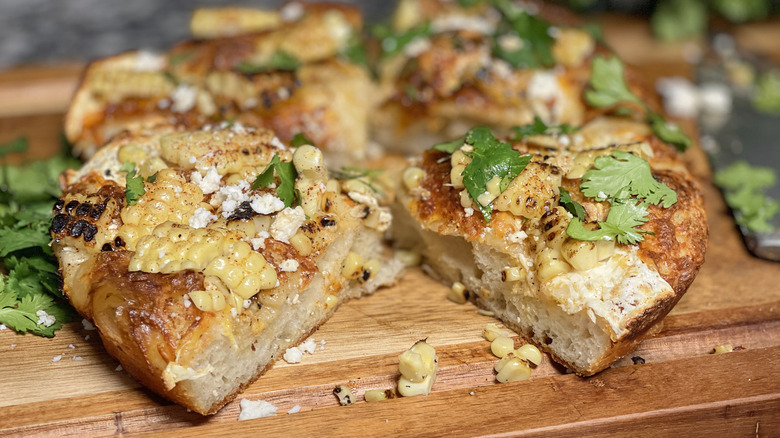 sliced cheesy elotes street corn pizza on cutting board