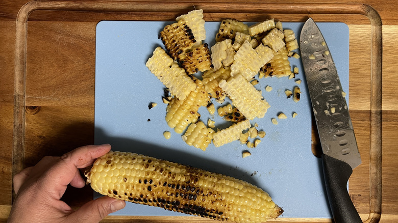 slicing off corn kernels onto cutting board