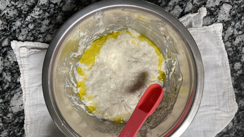 adding tablespoon of oil to wet dough in bowl