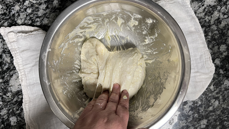 hand stretching dough in bowl