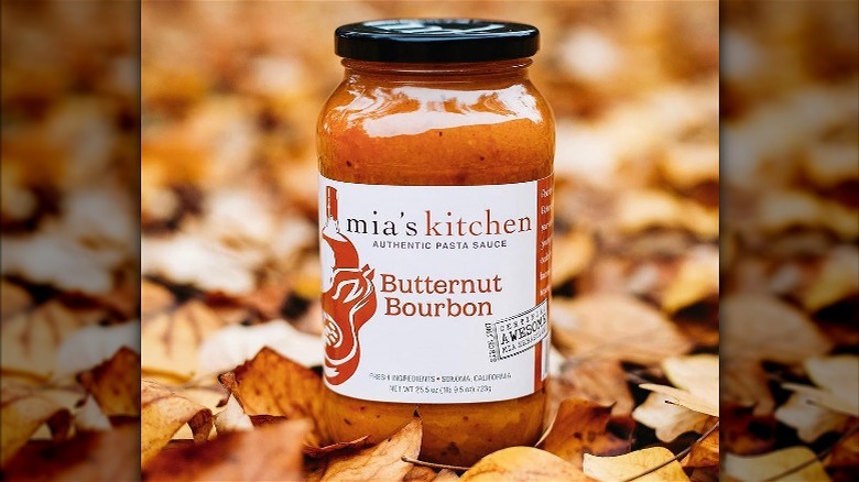 a jar of mia's butternut bourbon pasta sauce sitting in a pile of autumn leaves