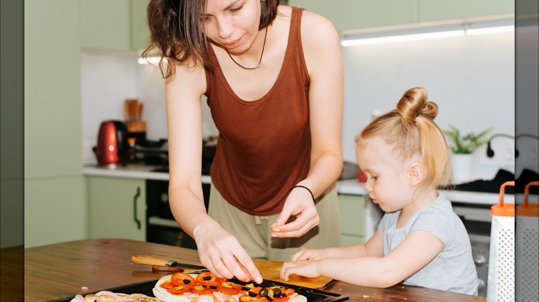 Mom and daughter topping pizza