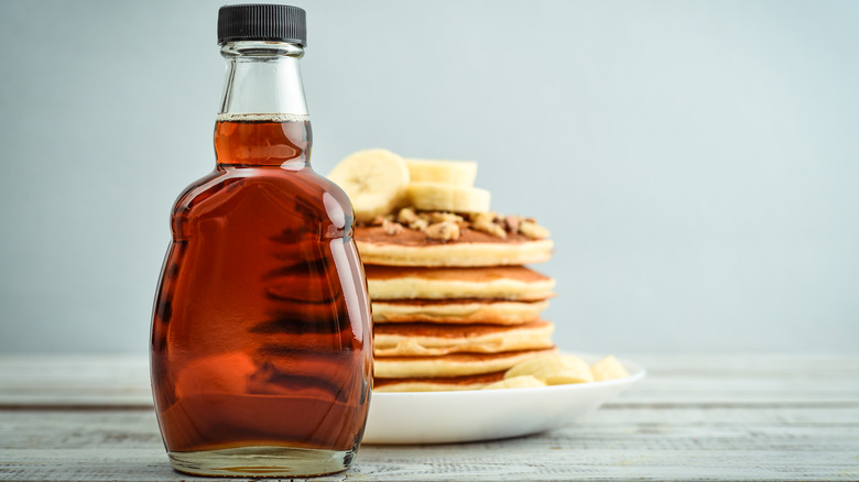 bottle of maple syrup in front of stack of pancakes