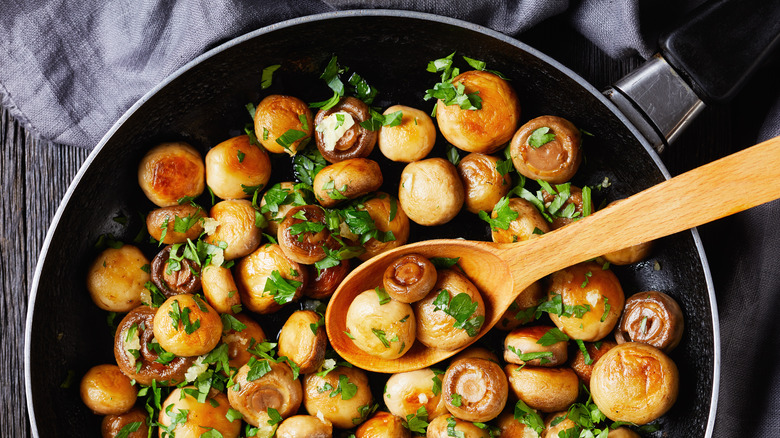 Saute mushrooms in pan with wooden spoon