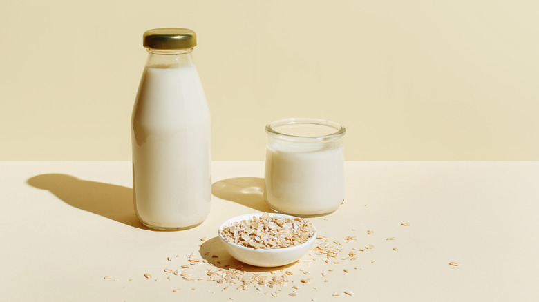 Bottle and glass of oat milk on beige background