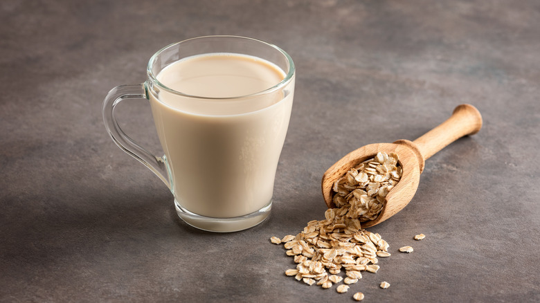 Glass of oat milk and scoop of oats on gray background