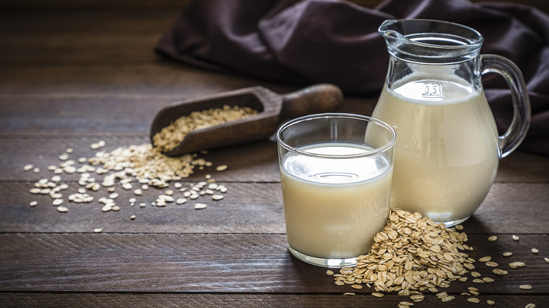 Carafe and cup of oat milk on wooden table with oats