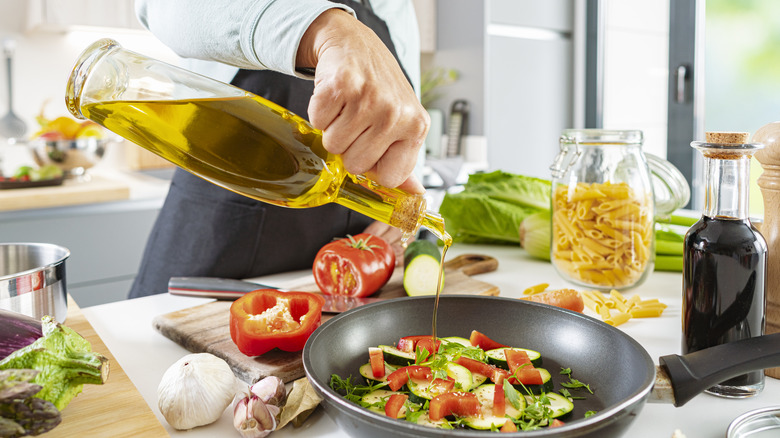 person pours olive oil into pan