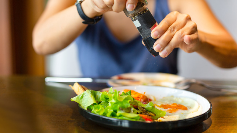 person grinding pepper over food