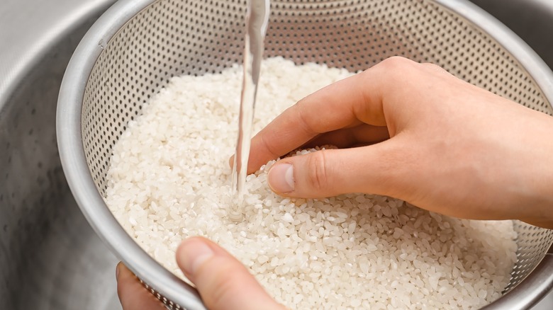 Person rinsing rice in metal strainer