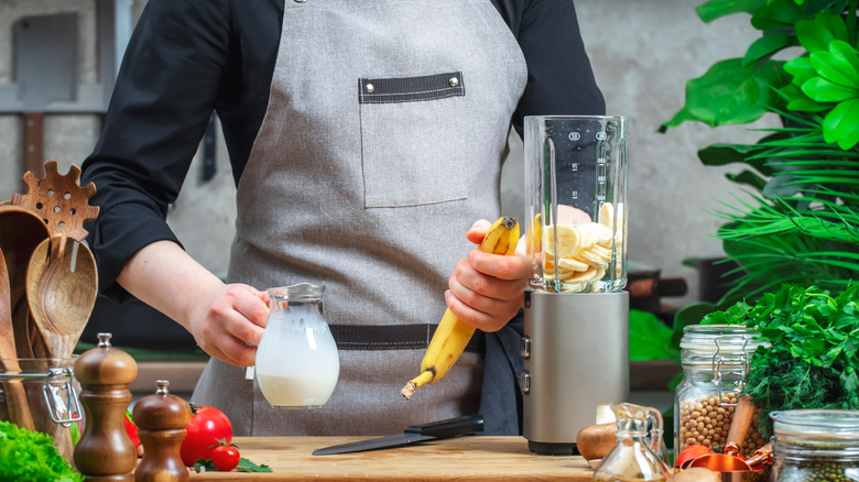 person makes smoothie with milk and banana