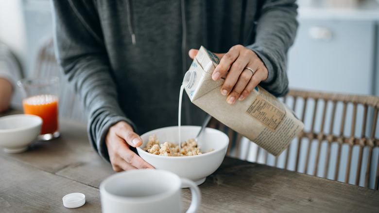 person pours soy milk into cereal