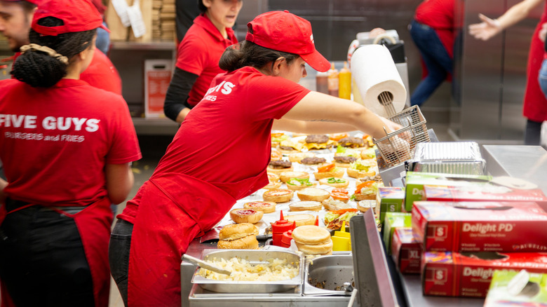 Young woman working in a Five Guys fast food chain in London. Ketchup, hamburgers and french fries.