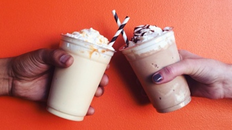 two hands holding milkshakes