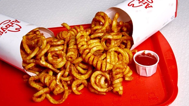 Two containers of Arby's curly fries are spilled together on a tray.